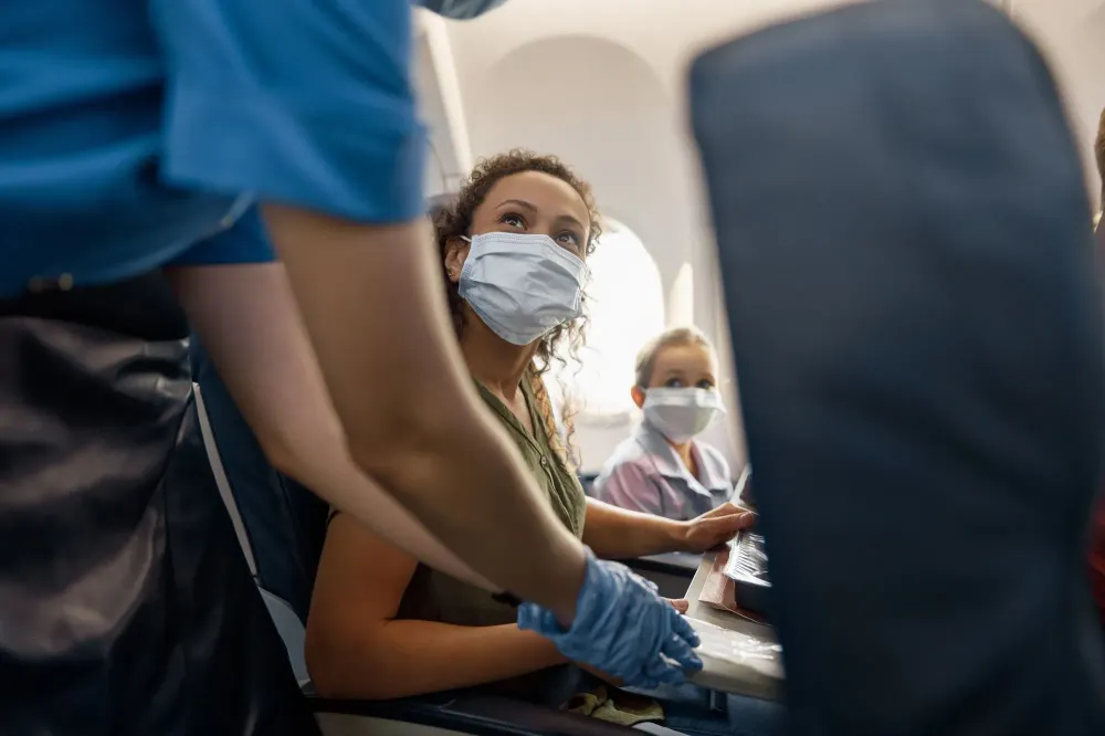 Woman and child wearing masks on plane speaking to a flight attendant